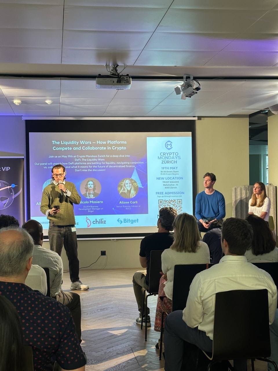 Gio Georgiou on stage with a microphone, opening a CryptoMondays Zurich panel