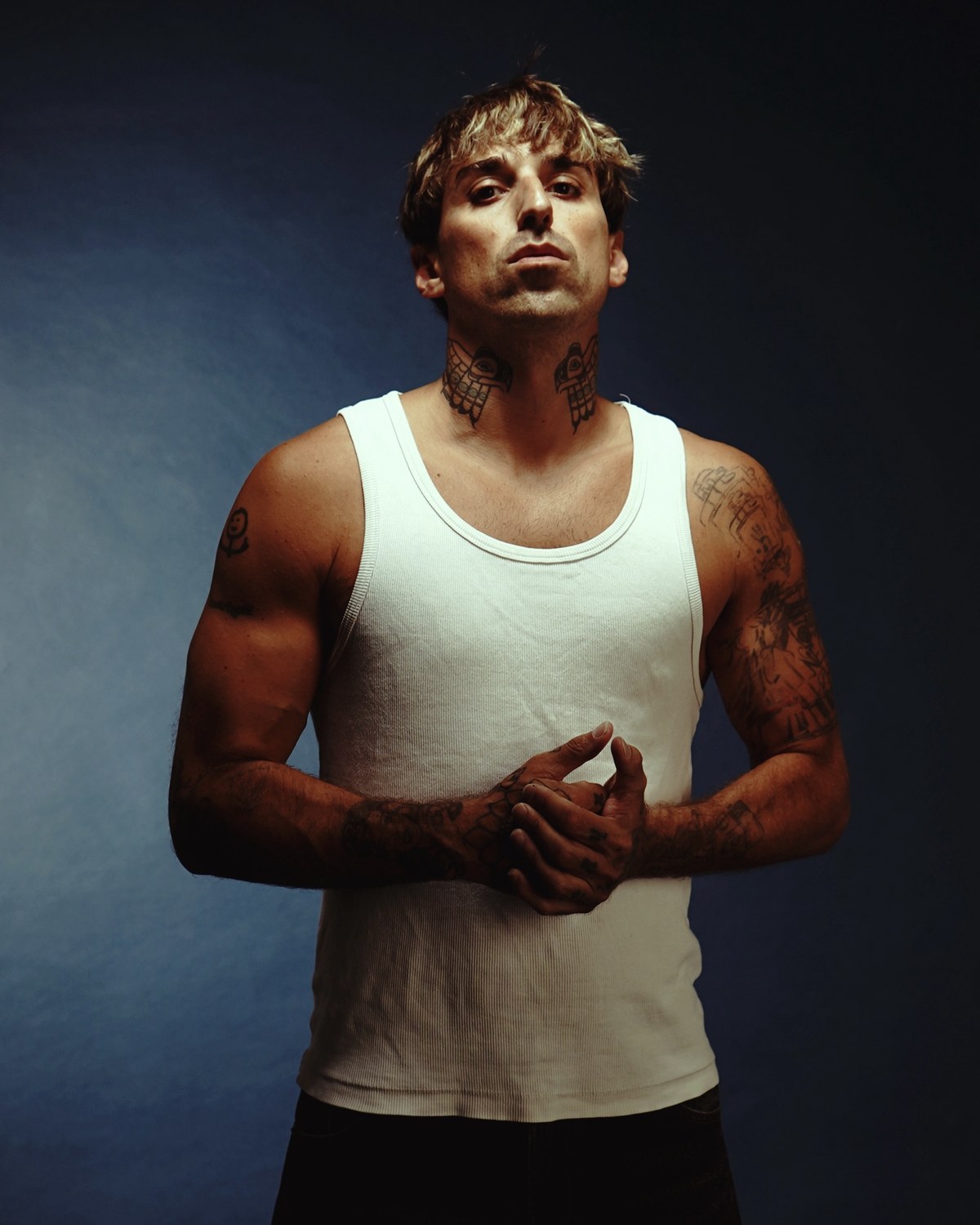 Gio Melody, studio portrait in a white tank top against a deep blue background
